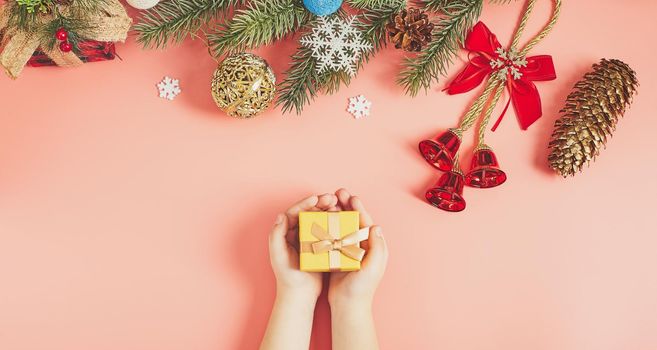 The child is holding a New Year's gift on a pink background with New Year's decorations.