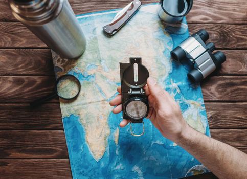 Man holding a compass over a map and planning to travel, point of view. Focus on the compass. The map is blurred