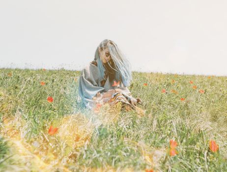 Beautiful young woman with blue hair rests on red tulips meadow on sunny day.