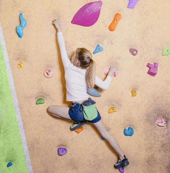 Little girl free climbing on artificial wall in gym, bouldering.