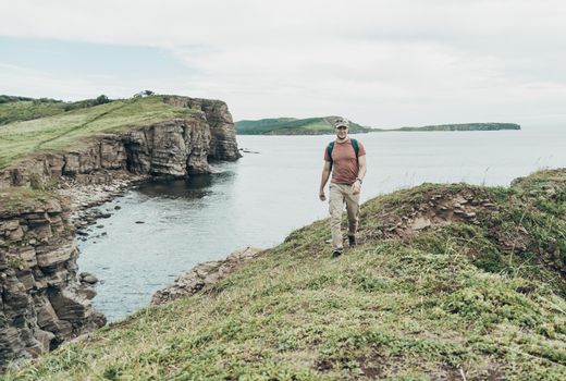 Traveler young man walking on high coastline on background of sea.