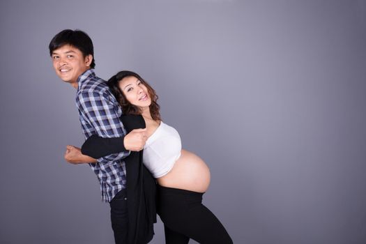 young couple: pregnant mother and happy father on gray wall background