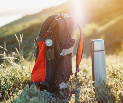 Travel equipment in the mountains: backpack, compass, binoculars and thermos.