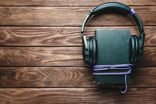 Headphones and book on a wooden background, top view, copy-space. Concept of audiobook.