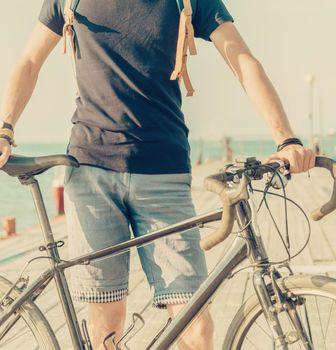 Unrecognizable young man standing with bicycle on coastline. Toned image.