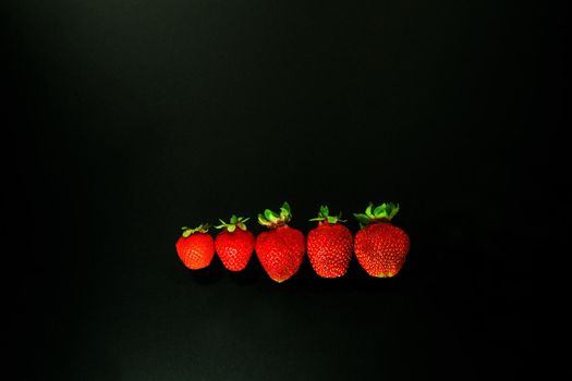 red strawbery on black background. red strawwberies ina line