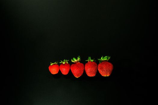 red strawbery on black background. red strawwberies ina line