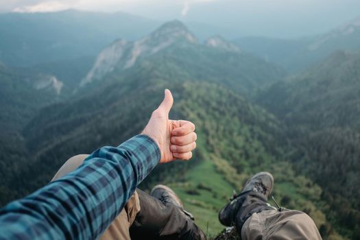 Traveler young man sitting in summer mountains and showing thumb up gesture, point of view shot.