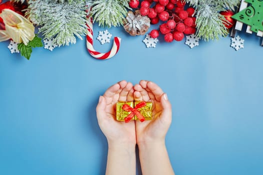 Girl holding a gift on a New Year's background. Children are waiting for gifts ,Christmas tree lights, pine branches, red winter berries and snow. Top view.