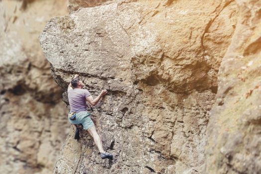 Young man free climbing on rock wall outdoor, extreme sport.