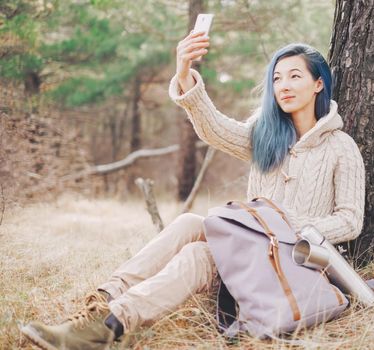 Explorer young woman with backpack taking selfie with smartphone in the forest.