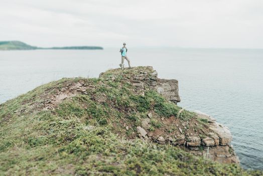 Explorer young woman standing on peak of cliff on background of sea.