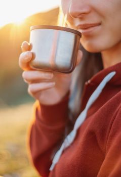 Young woman drinking tea from thermos cup outdoors, clouseup.