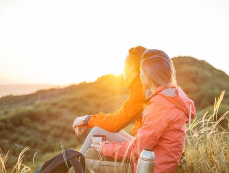 Traveler young couple resting in summer mountains at sunset and enjoying view of nature.