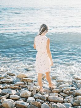 Young woman walking on pebble shore near the sea.