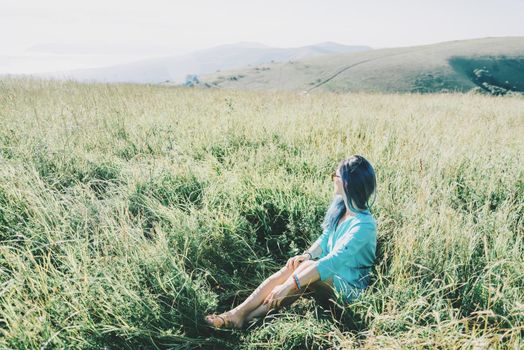 Young woman wearing in blue dress resting on summer meadow.