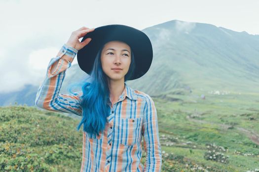Beautiful young woman with blue hair wearing in a hat walking in summer mountains.