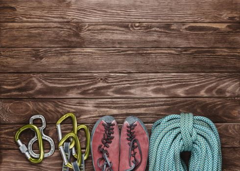 Climbing outfit: shoes, rope with carbines on wooden background, top view. Space for text in upper part of image.