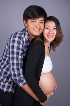 young couple: pregnant mother and happy father on gray wall background