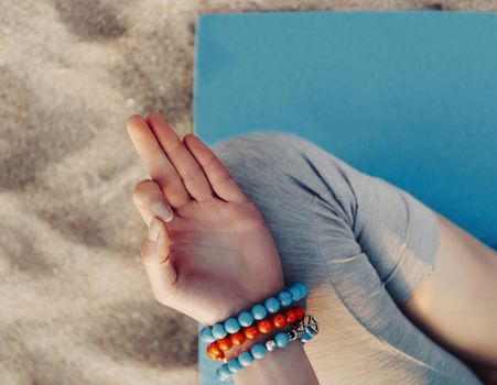 Young woman meditating in lotus position on beach, top view. Close-up of female hand.