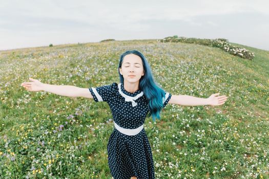 Beautiful young woman wearing in dress standing with raised arms on wildflower summer meadow, front view.