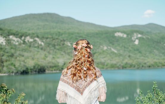 Beautiful woman with curly hairstyle enjoying view of nature in summer, rear view.