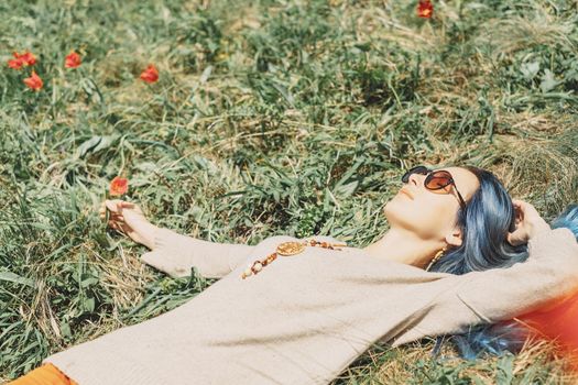 Beautiful young woman with blue hair lying on flower meadow.