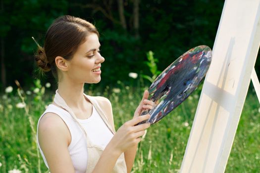 woman artist outdoors with palette of paints paints a picture. High quality photo