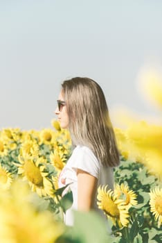 Beautiful woman standing in the field among yellow sunflowers.