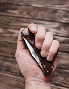 Male hand holding stainless jackknife on a wooden background.