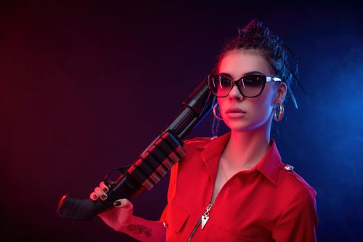bright brunette in a red jumpsuit with a shotgun on a dark background in neon light