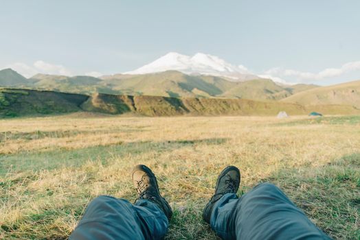 Hiker young man sitting in front of mountain Elbrus in summer, point of view.