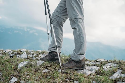 Female hiker with trekking poles walking in the rocky mountains, view of legs.