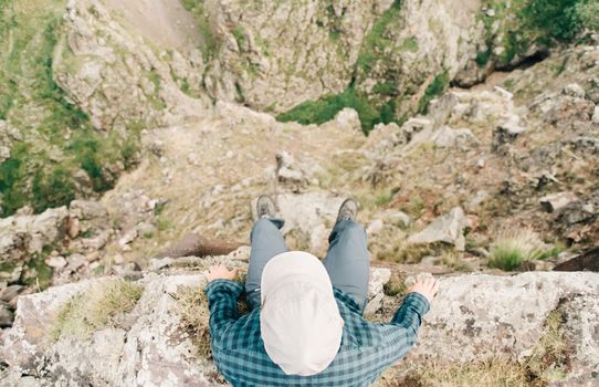 Explorer young man sitting on edge of cliff over canyon, top view.