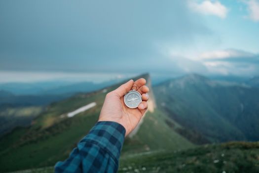 Male traveler holds a compass on background of mountains in summer, view of hand, pov.