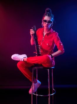 bright brunette in a red jumpsuit with a shotgun on a dark background in neon light