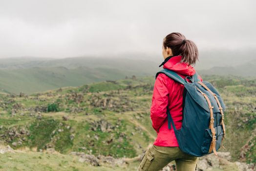 Explorer young woman with backpack walking in summer mountains.
