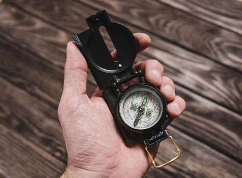 Male hand holding travel compass on a wooden background.