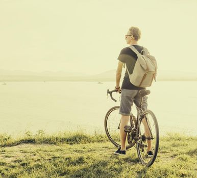 Young man with bike standing on coast and looking at sea. Toned image.