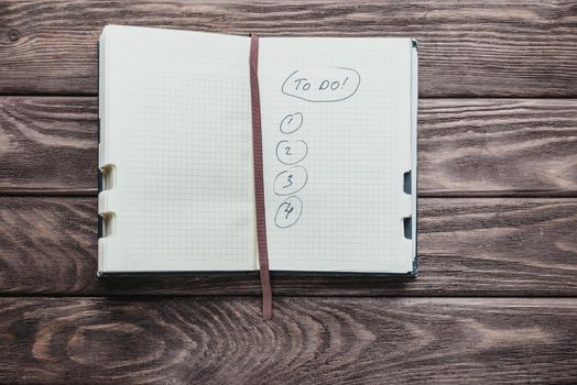 Notebook with to do list on a wooden background, top view.