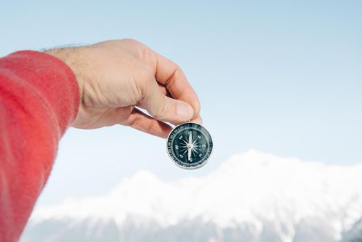 Male hand holding compass on background of snowy mountains, point of view.