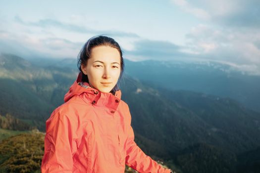 Explorer young woman standing on background of mountains in summer, looking at camera.