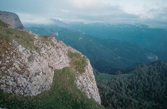 Traveler standing on rocky mountain in summer outdoor. Minimal person in massive landscape.