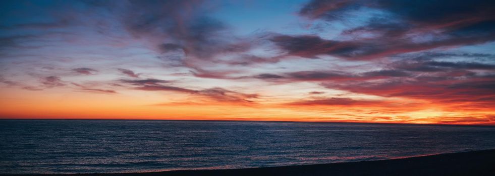 Beautiful sunset over sea in red and yellow colors, cloudy sky.