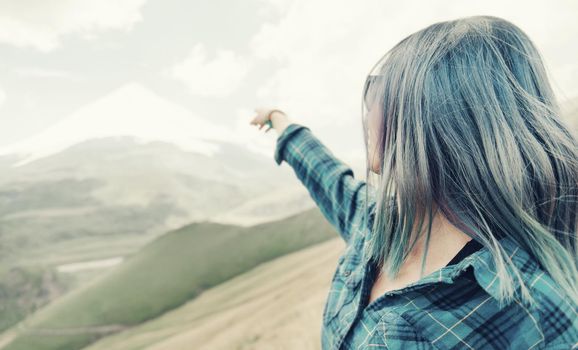 Young woman pointing at high mountain with snowy peak in the distance.