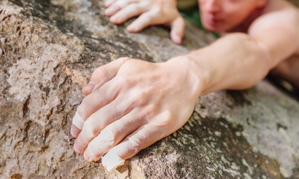 Young man climbing on rock wall, close-up of male hands with tape in magnesium powder.