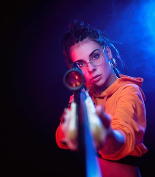 a beautiful brunette in an orange jumpsuit with a sniper rifle on a dark background and neon lights