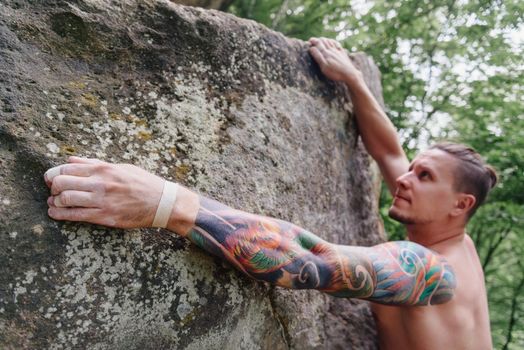 Young man with tattoo on his arm climbing on rock boulder in summer outdoor.