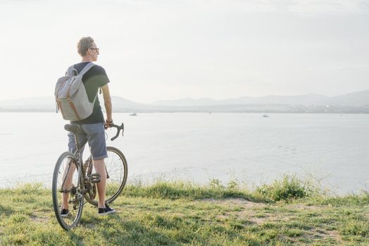 Young man with bicycle standing on coast and enjoying view of sea.
