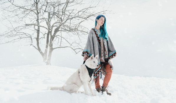 Beautiful boho style young woman with blue hair standing with Husky dog in winter outdoor.